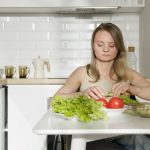 Woman sitting at table preparing fresh vegetables in a modern kitchen, highlighting healthy living and independence.